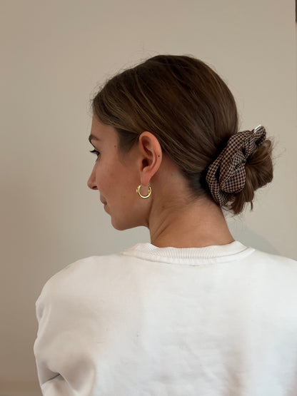 Eine Frau trägt ein braun-beige kariertes Drahthaarband im Hahnentrittmuster in Form eines Dutts.