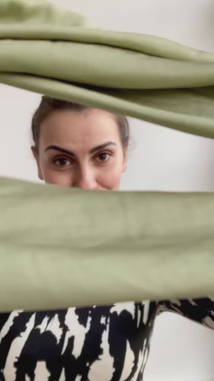 Video laden: Vor einem weißen Hintergrund bindet sich eine Frau mit einem grünen Drahthaarband eine Duttfrisur.