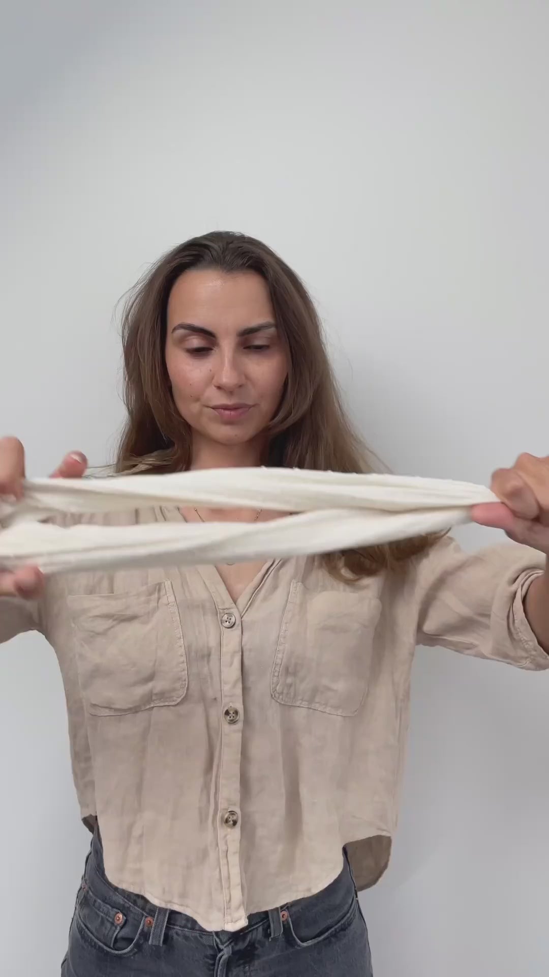Video laden: Vor einem weißen Hintergrund bindet sich eine Frau mit einem cremefarbenen Drahthaarband eine Duttfrisur.