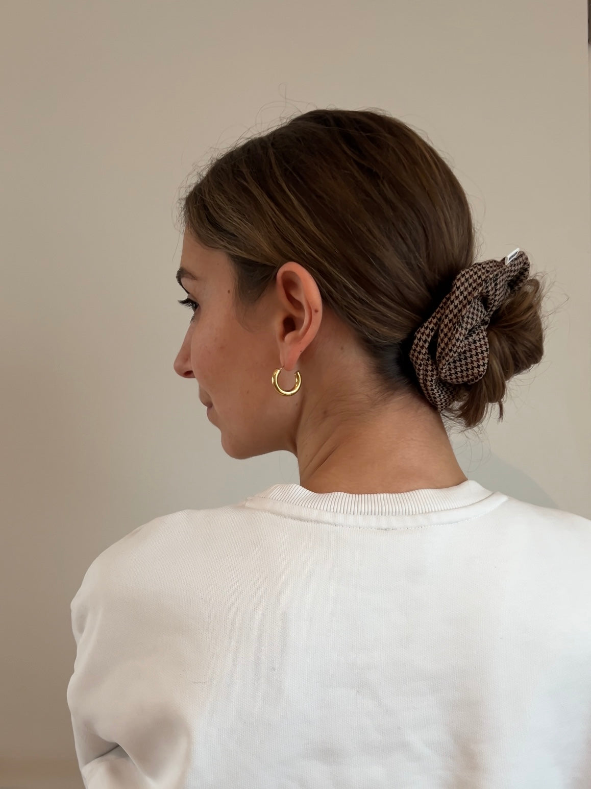 Eine Frau trägt ein braun-beige kariertes Drahthaarband im Hahnentrittmuster in Form eines Dutts.