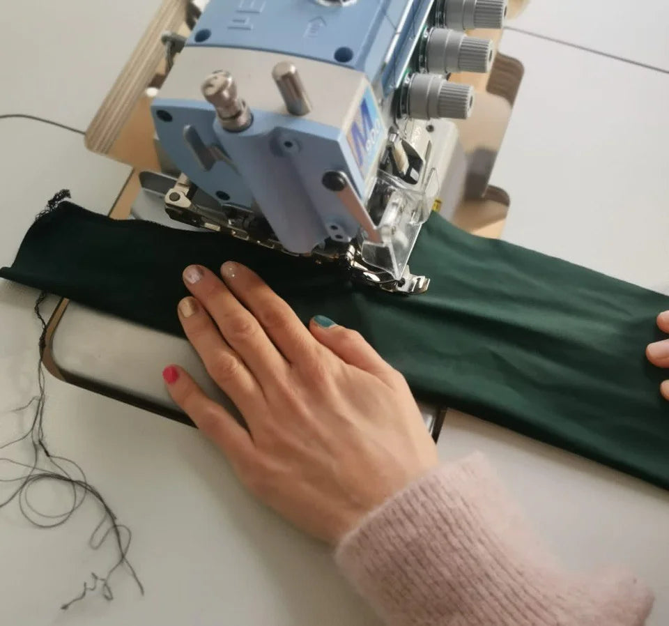 Es sind die Hände einer Schneiderin zu sehen, die mit ihrer Nähmaschine ein grünes Haarband näht.